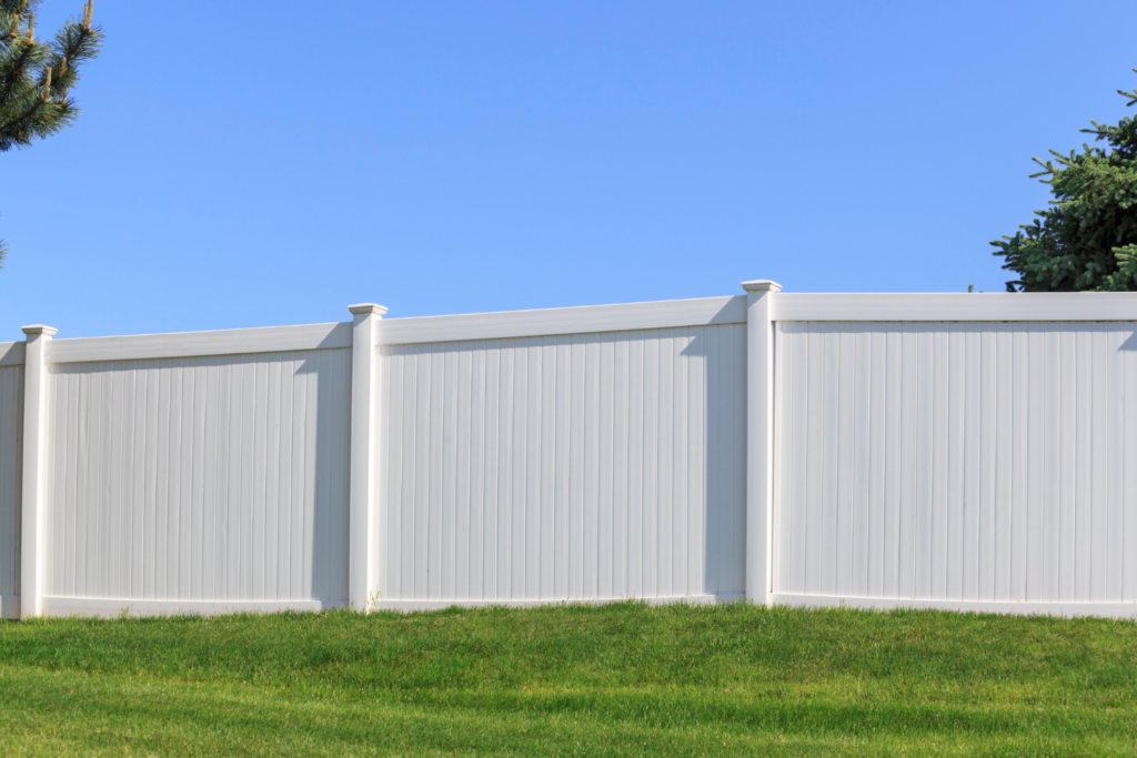 White vinyl privacy fence installed on a green lawn under a clear blue sky, showcasing Alpine Fence Company's durable and stylish fencing solutions.